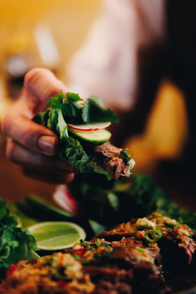 A hand holds a lettuce wrap filled with grilled meat, cucumber, radish, and coriander, a Providore Global dish.