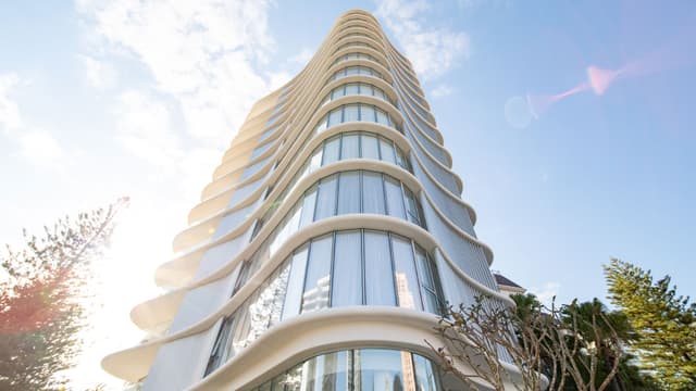 A curved white high rise apartment tower with glass balconies rises against a blue sky, an Usher Group development.