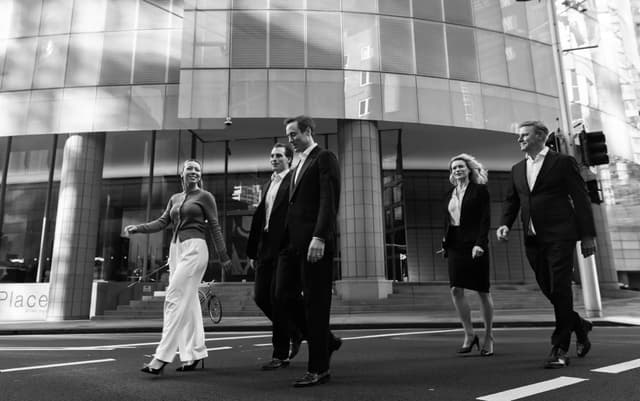 In black and white, five Vantage Asset Management colleagues in business attire cross a busy Melbourne CBD street.