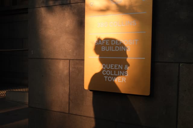 A building sign reading 380 Collins, Safe Deposit Building, Queen and Collins Tower, with a silhouette cast across it.