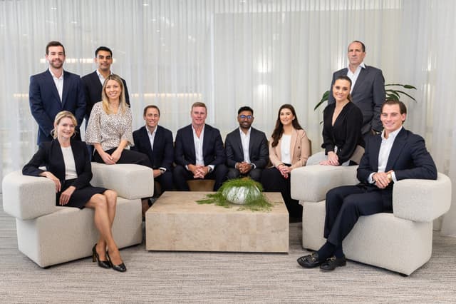 A large group of Vantage Asset Management colleagues in business attire pose together around a marble coffee table.