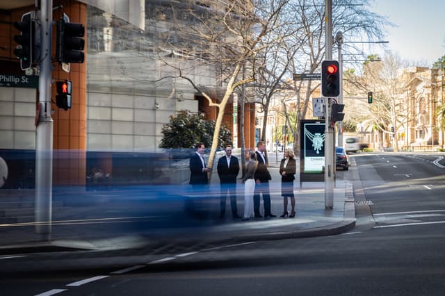 A long-exposure street photo shows five Vantage Asset Management colleagues standing at a Sydney CBD corner as traffic blurs past.