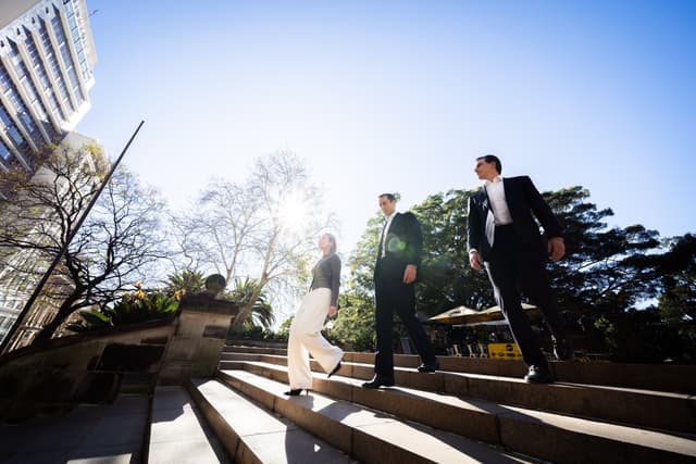 Three professionals in business attire walk down sunlit stone steps outside city buildings, for Vantage Asset Management.