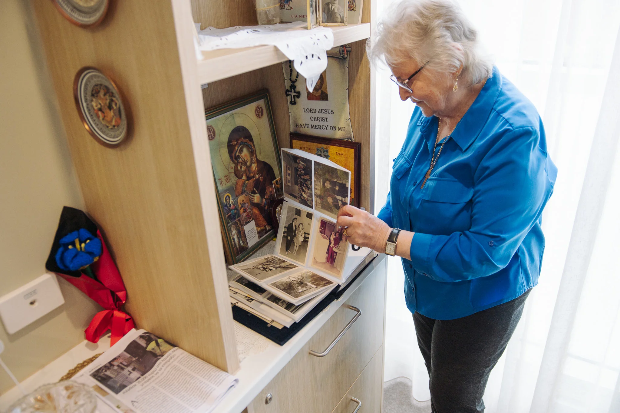 Georgia looking through family photographs beside the icons on her shelf at John Hood Terrace
