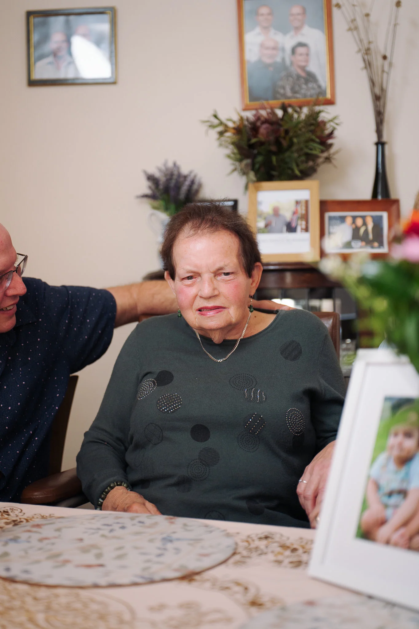Kelvin with his hand on his mum Lillian's shoulder at her dining table