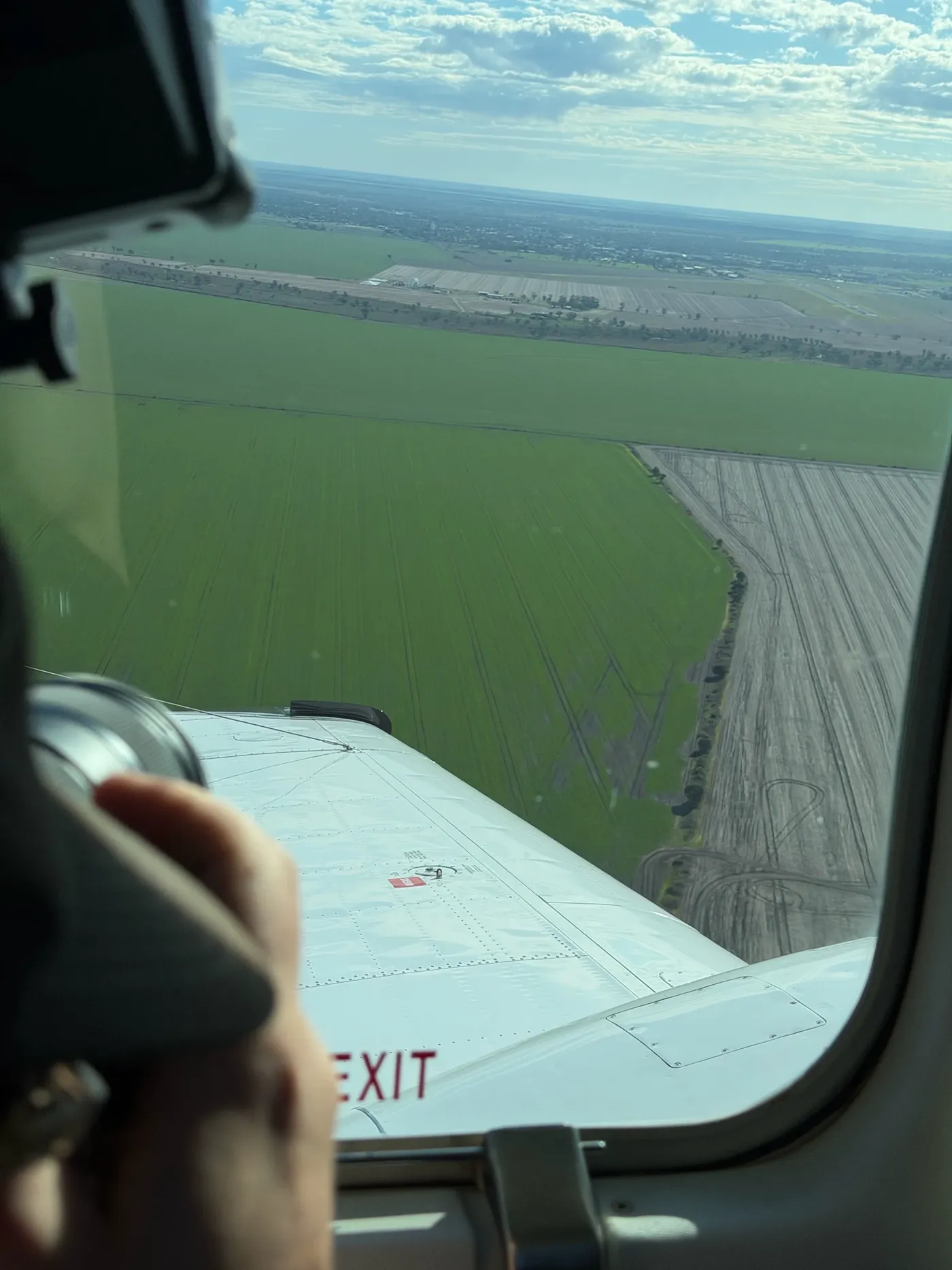 The wing of a light plane over green crop lines on approach to Moree