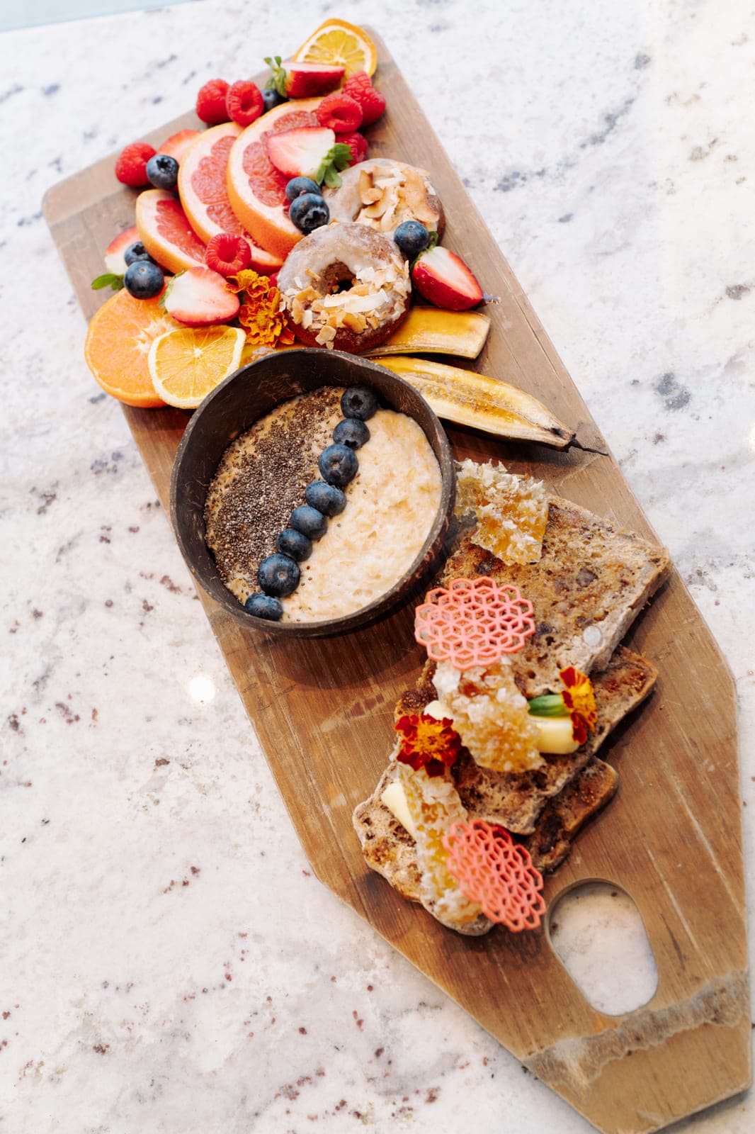 A breakfast grazing board of fruit, pastries and porridge on marble