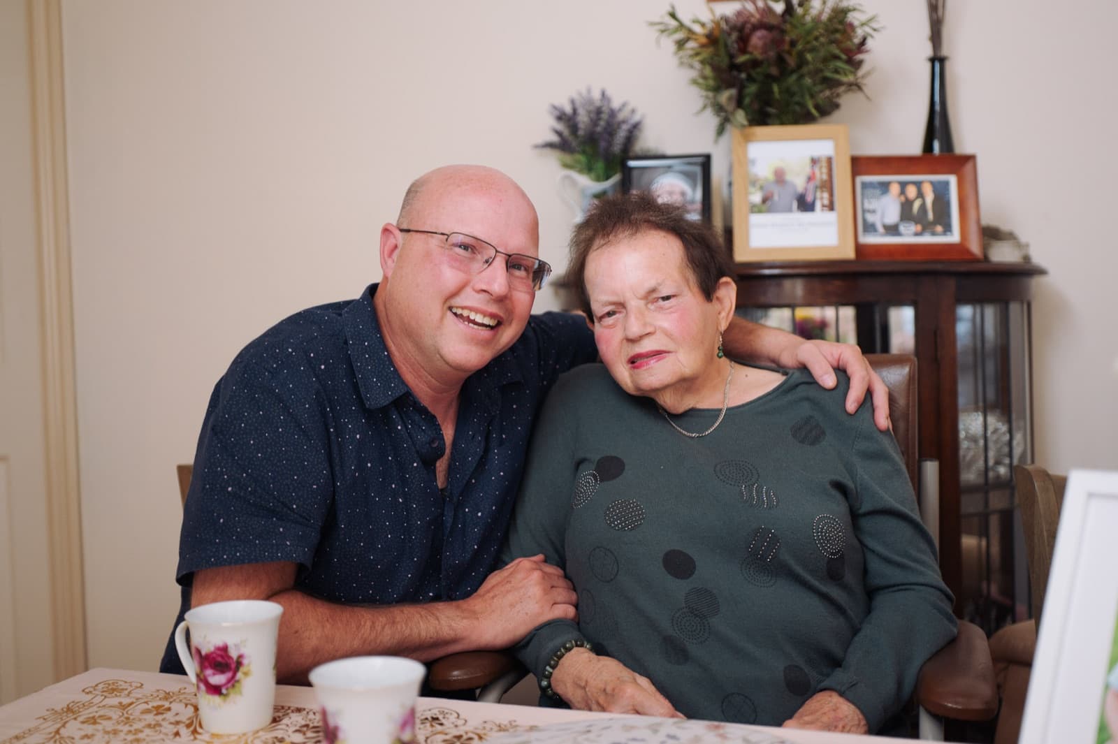 Kelvin with his arm around his mum Lillian at her dining table in Diamond Creek