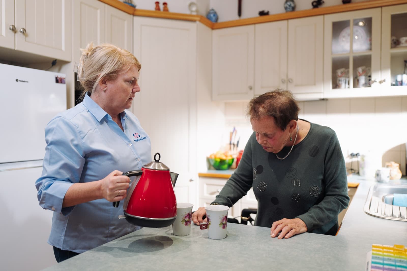 A mecwacare carer pouring tea for Lillian in her kitchen at home
