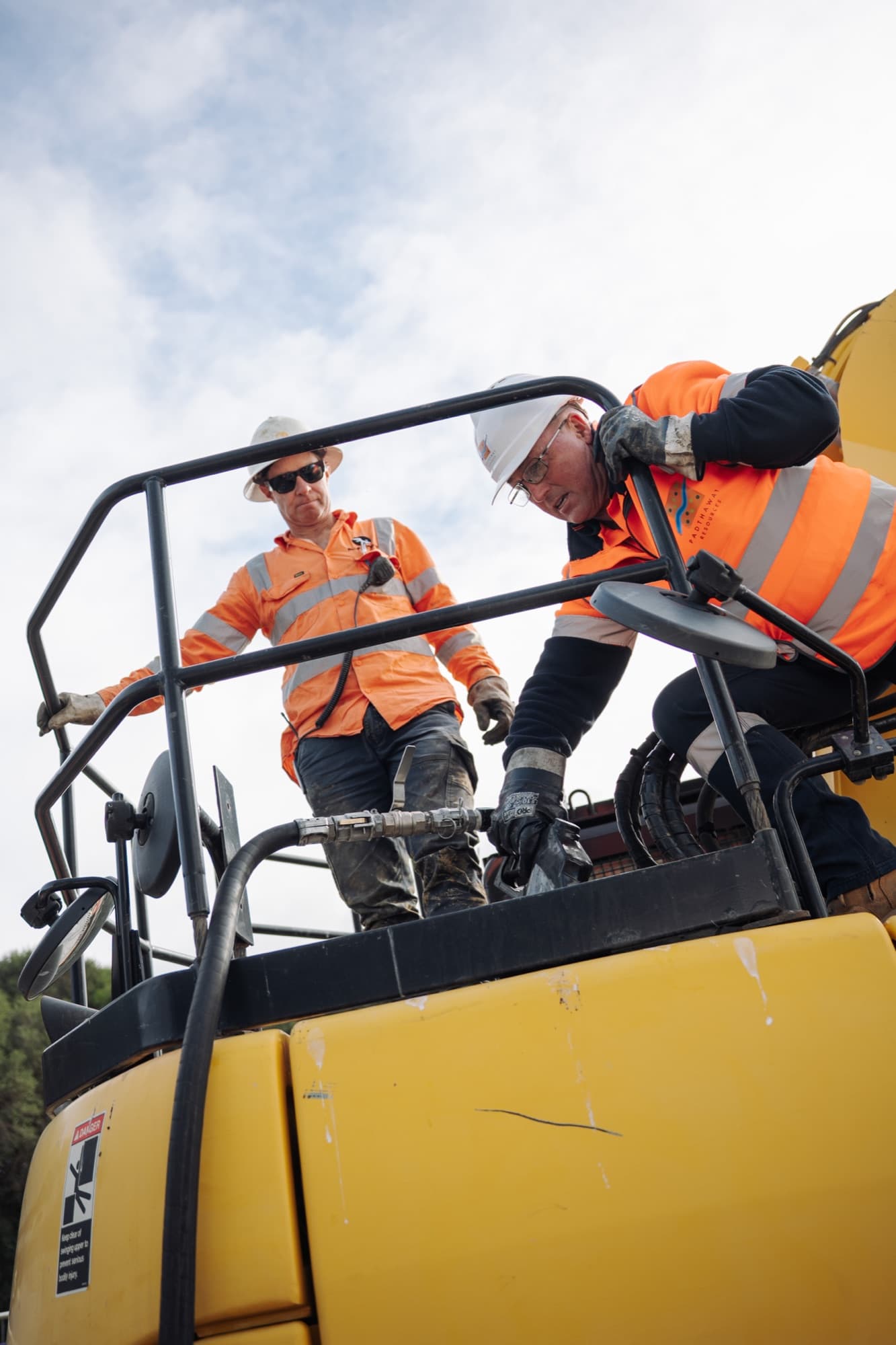 Two Padthaway operators in high visibility gear working on top of a plant machine.