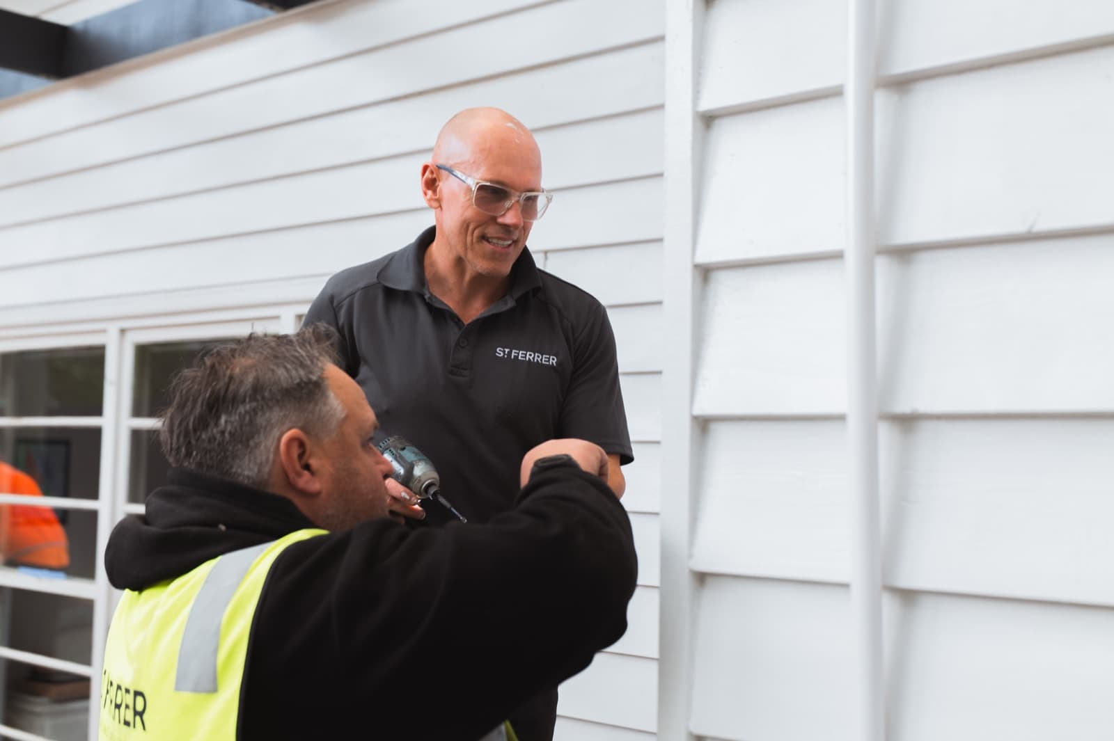 A St Ferrer director and a tradesperson sharing a laugh while working on the weatherboard cladding